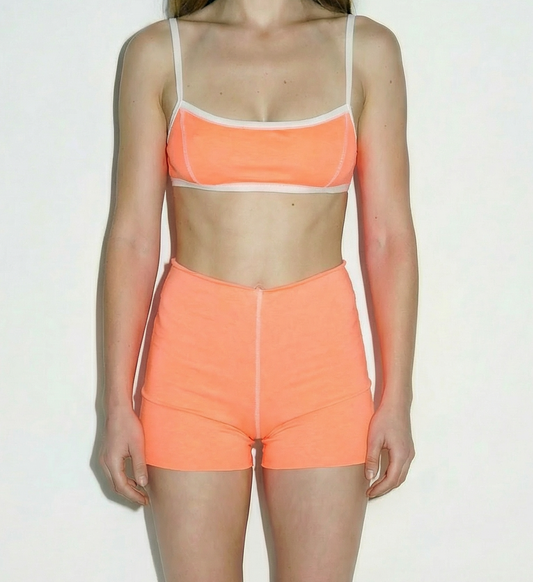 Woman wearing an orange sports bra and shorts set on a white background